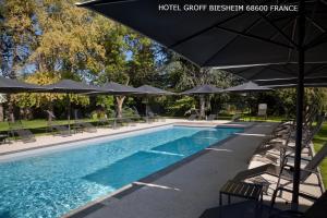 a large swimming pool with umbrellas and chairs and a pool at Aux Deux Clefs - Hôtel Restaurant Groff in Biesheim