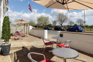 un patio con mesas, sillas y una sombrilla en Palm Court, Seafront Accommodation en Skegness