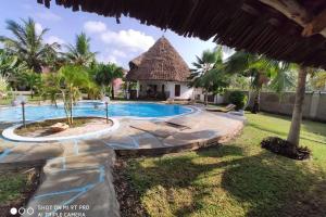 a resort swimming pool with a thatch roof at Dadida‘s Pool Cottage in Diani Beach