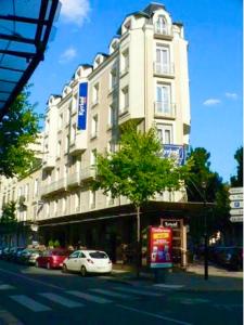een witte auto geparkeerd voor een hoog gebouw bij Kyriad Restaurant Centre SPA Vichy in Vichy