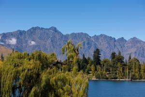 a tree in front of a lake with mountains in the background at Queenstown House Lakeside in Queenstown