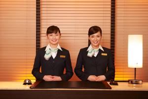 two women wearing suits and bow ties standing next to a table at Sotetsu Fresa Inn Ginza Sanchome in Tokyo