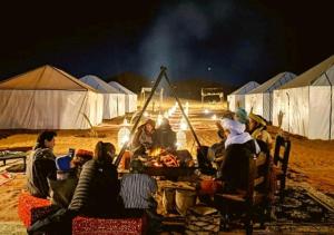 een groep mensen die 's nachts rond een kampvuur zitten bij Morocco Luxury Camp - Merzouga Desert Retreat in Merzouga