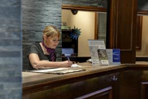 una mujer sentada en un escritorio escribiendo en un papel en Bury Ramsbottom Old Mill Hotel and Leisure Club en Ramsbottom