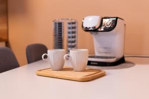 two coffee cups on a cutting board next to a juicer at Apartmány V Mlýnské strouze in Pilsen