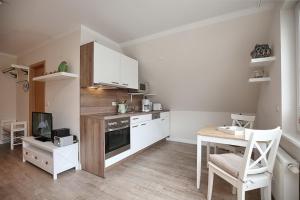 eine Küche mit weißen Schränken, einem Tisch und einem Herd in der Unterkunft Strandvilla Krabbe Wohnung 13 in Boltenhagen