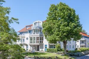 Una gran casa blanca con un árbol delante. en Dünenblick Wohnung 24, en Boltenhagen