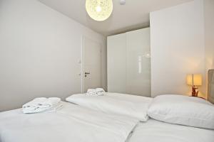 2 weiße Betten in einem weißen Schlafzimmer mit einem Kronleuchter in der Unterkunft Linden-Palais Wohnung 25 in Heiligendamm