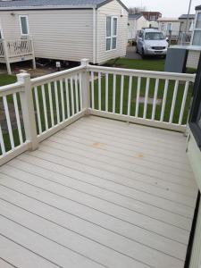 a wooden deck with a white railing and a house at Annandale skegness in Skegness
