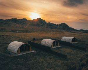 três cúpulas num campo com o pôr-do-sol ao fundo em Volcano Cabins em Acharacle