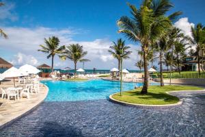 ein Pool in einem Resort mit Palmen und Stühlen in der Unterkunft Beach Class Muro Alto Condomínio Resort By New Time in Porto De Galinhas
