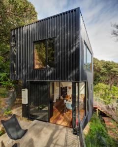 a black house on a deck with a table at Blackpool House in Oneroa