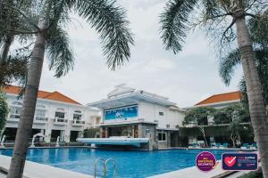 a hotel with a swimming pool and palm trees at Adhiwangsa Hotel in Solo