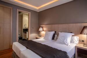 1 dormitorio con 1 cama grande con sábanas y almohadas blancas en Washington Parquesol Suites & Hotel en Valladolid