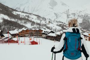 a woman with a backpack looking at a ski resort at Lodji Hotel & Résidence in Saint-Martin-de-Belleville