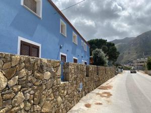 a blue building next to a stone wall at B&B Pelagos in Castellammare del Golfo
