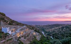 a house on a mountain with the ocean in the background at Tinos Dove Suites in Triandáros
