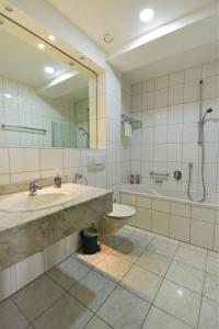 een badkamer met een wastafel, een bad en een spiegel bij LandhotelUllrich in Baumholder