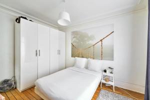 パリにあるCosy Apartment for 2 People near Pigalleの白いベッドルーム(ベッド1台付)が備わります。壁には絵画が飾られています。