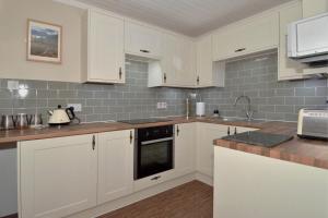 a kitchen with white cabinets and gray tiles at The Bridge Suite in Invermoriston
