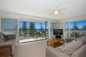 a living room with a couch and a television and a balcony at Solnamara Beachfront Apartments in Gold Coast