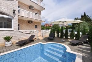 a swimming pool with chairs and an umbrella next to a building at Apartment House Jerko in Kaštela
