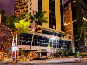 a building with a palm tree in front of a street at Grand Mercure Recife Boa Viagem in Recife