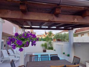 une terrasse avec une table, des chaises et des fleurs violettes dans l'établissement Apartments Benic, à Zadar