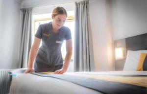 a woman making a bed in a hotel room at Maldron Hotel Manchester City Centre in Manchester