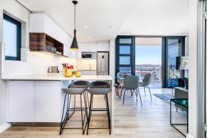 una cocina con armarios blancos y una barra con taburetes en Always-Power Luxury Sky Retreat, en Ciudad del Cabo