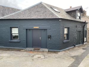 een zwart huis met een grijze deur en twee ramen bij holidayhomemoffat,com (Stable Cottage) in Moffat