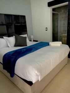 Una gran cama blanca con una manta azul. en Thamani Guest House en Randfontein