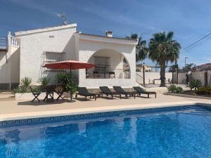 a pool with chairs and an umbrella next to a house at Casa Giner in Ciudad Quesada