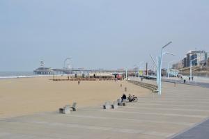 a sandy beach with people sitting on benches and a pier at Hotel De Stern in Scheveningen