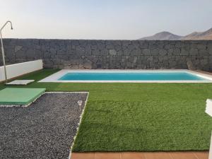 una piscina con césped y una pared de piedra en Luxury Villa Lanzarote, en Playa Blanca