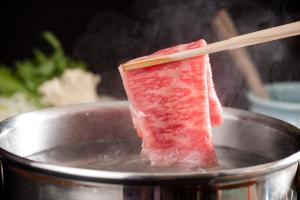 a piece of meat in a pan with a chopstick at Hotel Mt. Fuji in Yamanakako