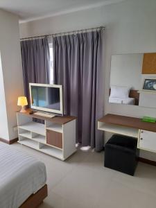 Schlafzimmer mit einem Bett und einem Schreibtisch mit einem TV in der Unterkunft The September Salaya in Salaya