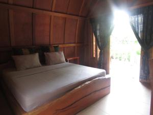 a bedroom with a white bed with wooden walls and a window at Bale Jukung in Tanjung