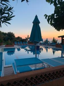 a swimming pool with an umbrella and chairs and a table at Villaggio Athragon in Capo Vaticano