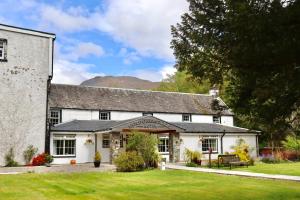 an old white building with mountains in the background at Rowardennan Hotel in Rowardennan