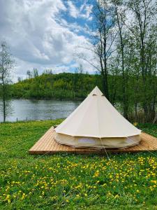 biały namiot siedzący na drewnianej platformie obok jeziora w obiekcie Murimäe Winery glamping w mieście Otepää