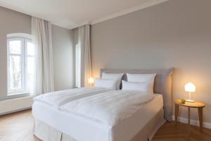 a white bedroom with a large white bed with two lamps at Vju Hotel Rügen in Göhren