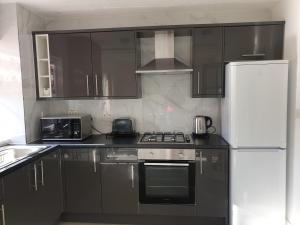 eine Küche mit schwarzen Schränken und einem weißen Kühlschrank in der Unterkunft JDB Dartford 2-Bedroom House in Dartford