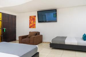 ein Schlafzimmer mit einem Bett und einem Stuhl sowie einem Flachbild-TV in der Unterkunft Hotel Casa Blanca Laureles in Medellín