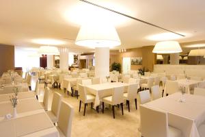 un comedor con mesas blancas, sillas y luces en Laguna Palace Hotel Grado en Grado