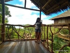 una mujer parada en un balcón de madera con vistas al bosque en Sanctuaria Treehouses Busuanga en Busuanga