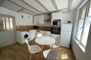 La cuisine est équipée d'une table et de chaises blanches ainsi que d'un réfrigérateur blanc. dans l'établissement Centre-ville : Maison de charme - Secteur calme, à Laval