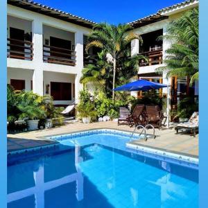 a swimming pool with chairs and an umbrella and a building at Pousada Vila Morena in Itaúnas