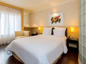 um quarto de hotel com uma grande cama branca e uma cadeira em Pullman Sao Paulo Ibirapuera em São Paulo