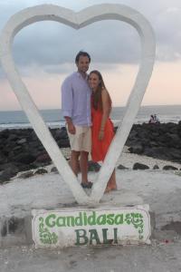 Un uomo e una donna in piedi sotto un cartello cardiaco sulla spiaggia di Ashyana Candidasa Beach Resort a Candidasa